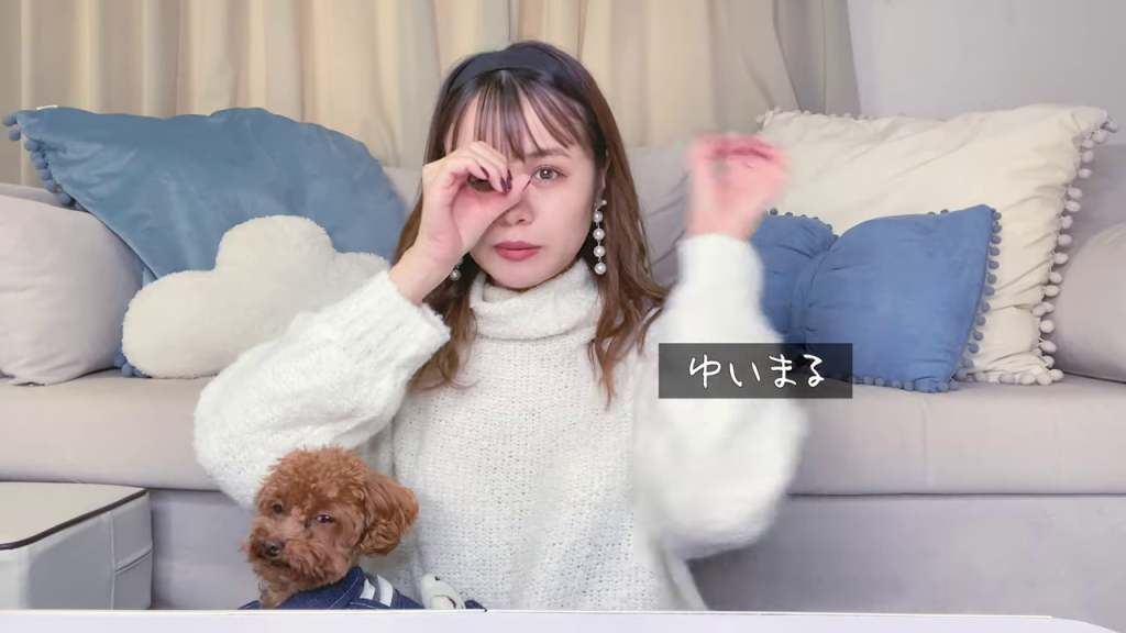 リビングで愛犬を膝に乗せ、両手でOKサインのようなポーズをとるアイヴァーンさん