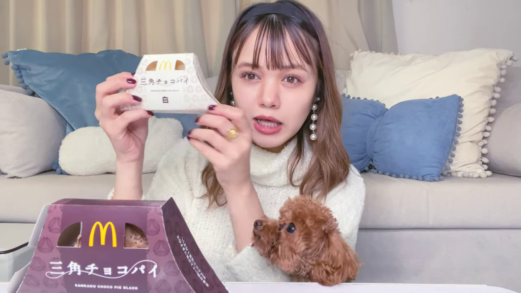 両手に「三角チョコパイ 黒」と「三角チョコパイ 白」のパッケージを持つアイヴァーンさん