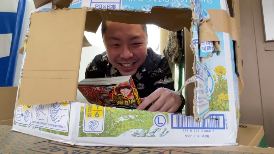 段ボールの中から笑顔で『ONE PIECE』を読む男性
