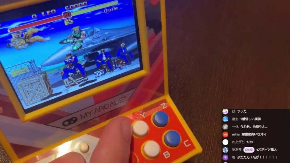 ミニアーケードゲーム機で「ストリートファイターII」をプレイしている指が映っている。