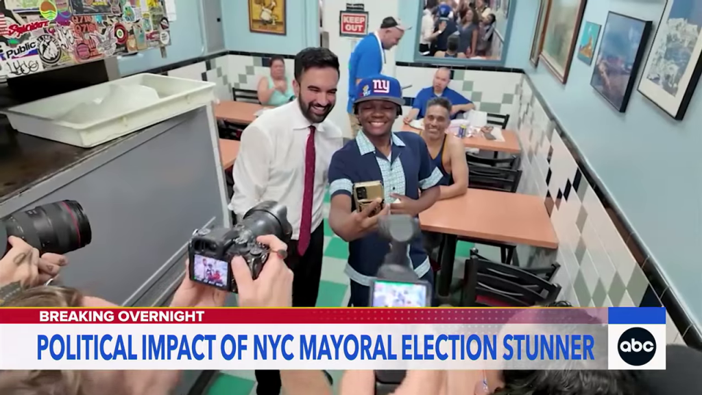 「PSC CUNY VOTES」看板を掲げる男性候補者と支持者