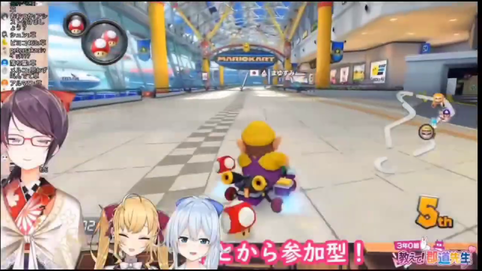 マリオカートの空港コースを走行するワリオと、アイテムを所持するゲーム画面、3体のVTuberアバターとチャット、テロップ。