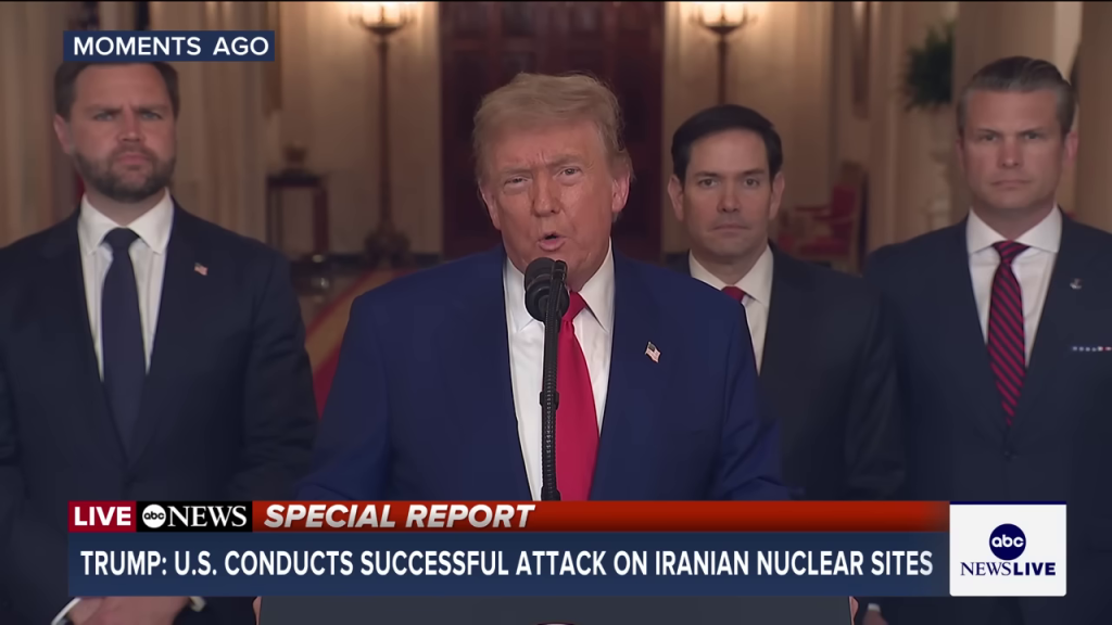 トランプ氏がマイクに向かってスピーチする様子。背景には補佐官らしき人物が立ち、下部には「TRUMP: U.S. CONDUCTS SUCCESSFUL ATTACK ON IRANIAN NUCLEAR SITES」というニューステロップが流れている。公式声明の緊迫した雰囲気を伝える。